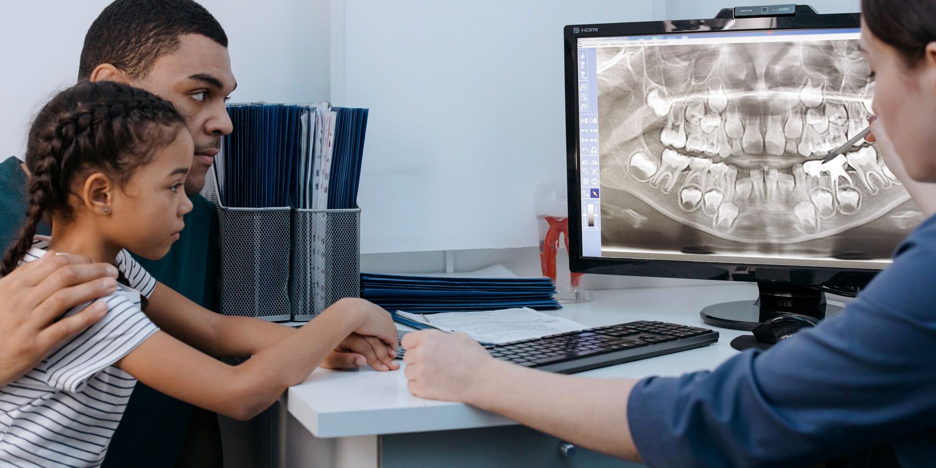 A dentist showing an x-ray on screen to a father and daughter