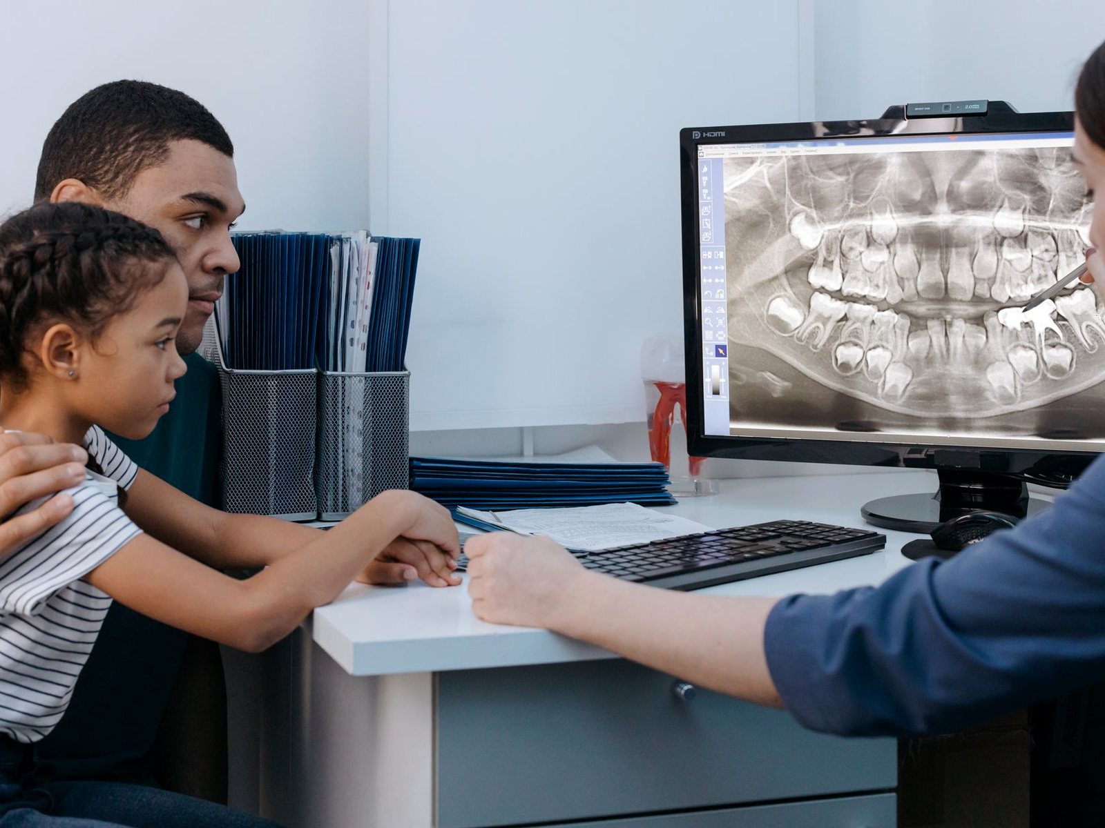 A dentist showing an x-ray on screen to a father and daughter